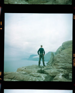 Rear view of man standing on rock against sky