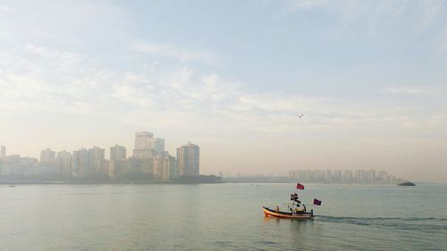 Boat moving in river by city against sky