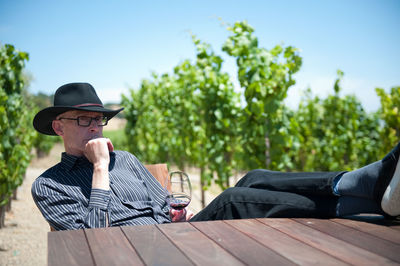 Thoughtful man with legs on table holding wineglass in vineyard