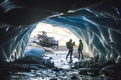 Man photographing partner in ice cave during helicopter tour.