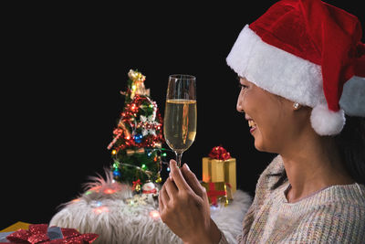 Smiling woman holding champagne flute against black background during christmas
