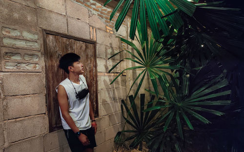 Young man looking away while standing against wall