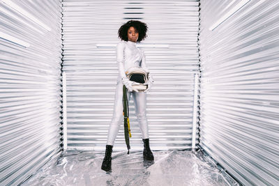 Charming african american female with helmet in white astronaut costume looking at camera while standing in white spaceship on light background