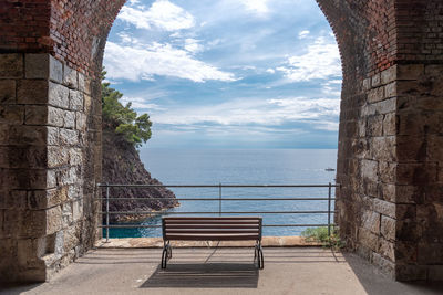 Empty bench by sea against sky