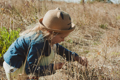 Adorable little girl in straw hat in the field collecting wild grass. stylish child countryside