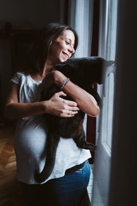 Young pregnant woman at home holding a black cat on shoulder