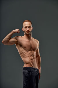 Portrait of shirtless man with arms crossed standing against sky