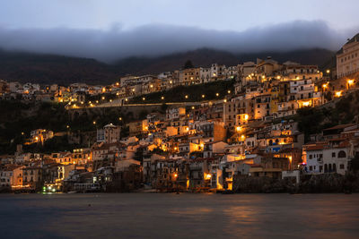 Illuminated buildings by sea against sky at night