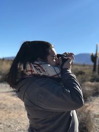 Side view of woman photographing from camera on land against clear sky