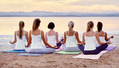 Rear view of female friends doing yoga at beach during sunrise