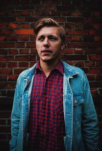 Portrait of young man standing against brick wall