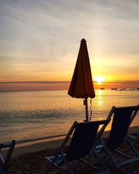 Chair on beach against sky during sunset