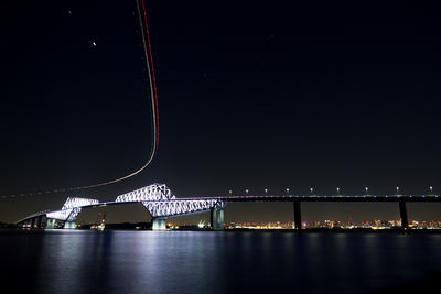 Illuminated bridge over river against sky at night