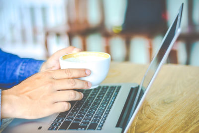 Close-up of businessman using laptop while drinking coffee on table