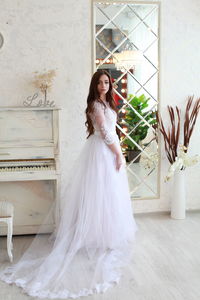 Portrait of young bride standing against wall at home