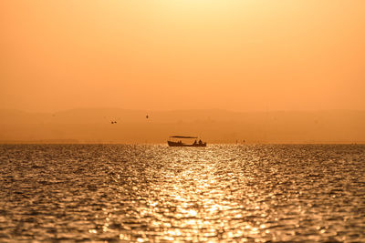 Silhouette boat in sea against orange sky