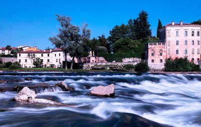 Water flowing by buildings in city against blue sky