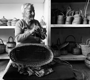 Woman making wicker baskets while sitting on table at home