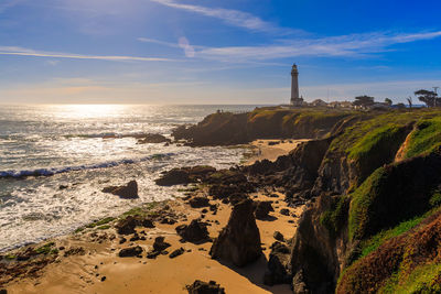 Lighthouse by sea against sky during sunset