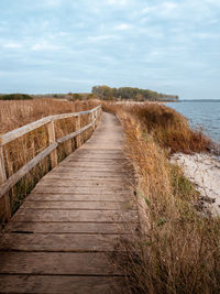 Footpath leading towards sea against sky