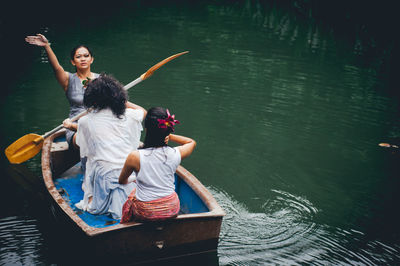 Full length of friends sitting on boat sailing in river