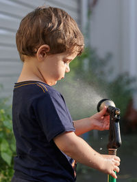 Little boy playing with a watering hose in the backyard