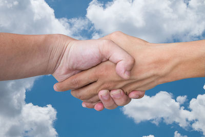 Cropped image of people shaking hands against cloudy sky