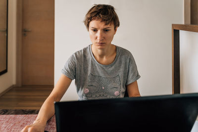 A woman in home clothes works at home at laptops with a tense look