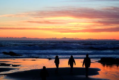 Silhouette people on beach against sky during sunset