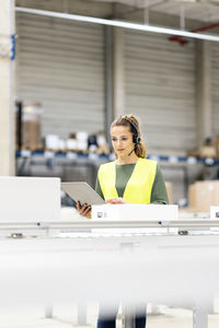 Worker wearing headset holding tablet pc examining box on conveyor belt in warehouse