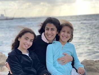 Portrait of mother with two young girls daughters sitting near the beach sea