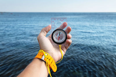 A man's hand with a wristwatch bracelet holds a magnetic compass against the background of the sea