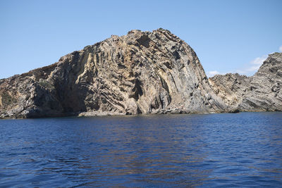 Rock formations in sea against clear blue sky