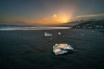 Iceberg on shore at beach against sky during sunset