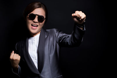 Portrait of young woman wearing sunglasses against black background