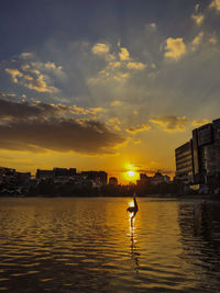 Scenic view of river by buildings against sky during sunset