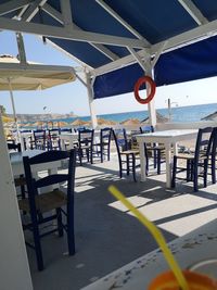 Empty chairs and table on beach against sky