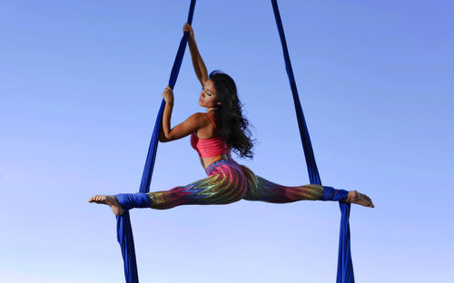 Full length of young woman with fabrics dancing against blue sky