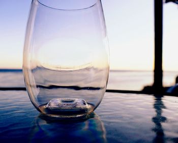 Close-up of empty glass on reflective table against sky