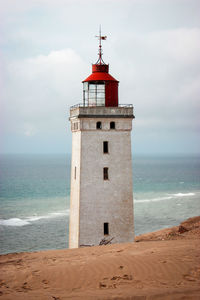 Lighthouse on beach by sea against sky