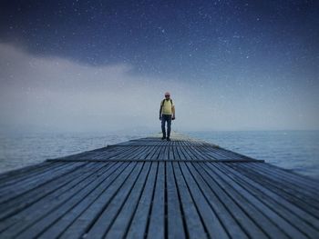 Man standing on pier over against sky at night