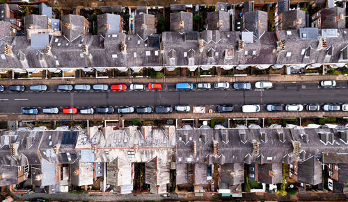 Aerial view above rooftops of back to back terraced houses on suburban street with parked cars