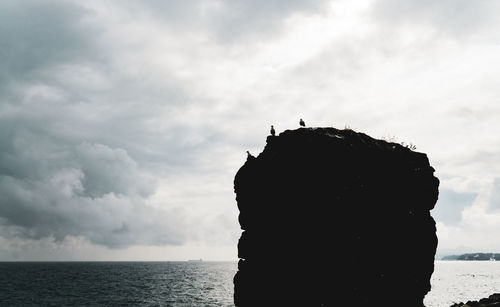 Silhouette rock formation by sea against sky