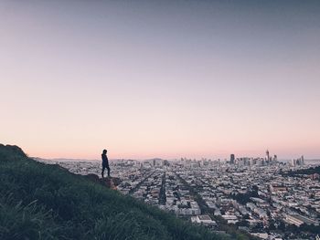 Woman standing on mountain overlooking cityscape against sky during sunset