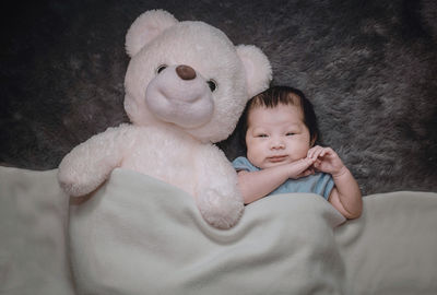 Portrait of cute baby girl lying by teddy bear on bed