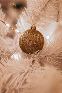 Golden christmas ball hanging on the white christmas tree. magic cozy details. winter holidays 