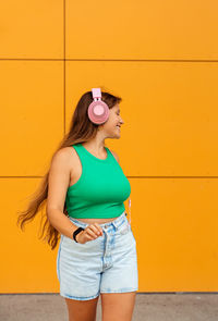 Portrait of young woman standing against yellow wall