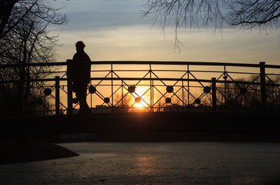 Silhouette man standing by railing on bridge over river during sunset