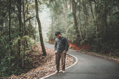 Portrait of man standing on road amidst trees in forest