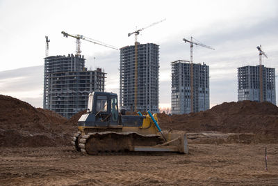 Cranes at construction site in city against sky